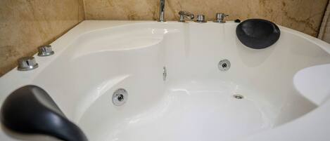 A white bathtub with a black seat, a handheld showerhead, and a black soap dish.