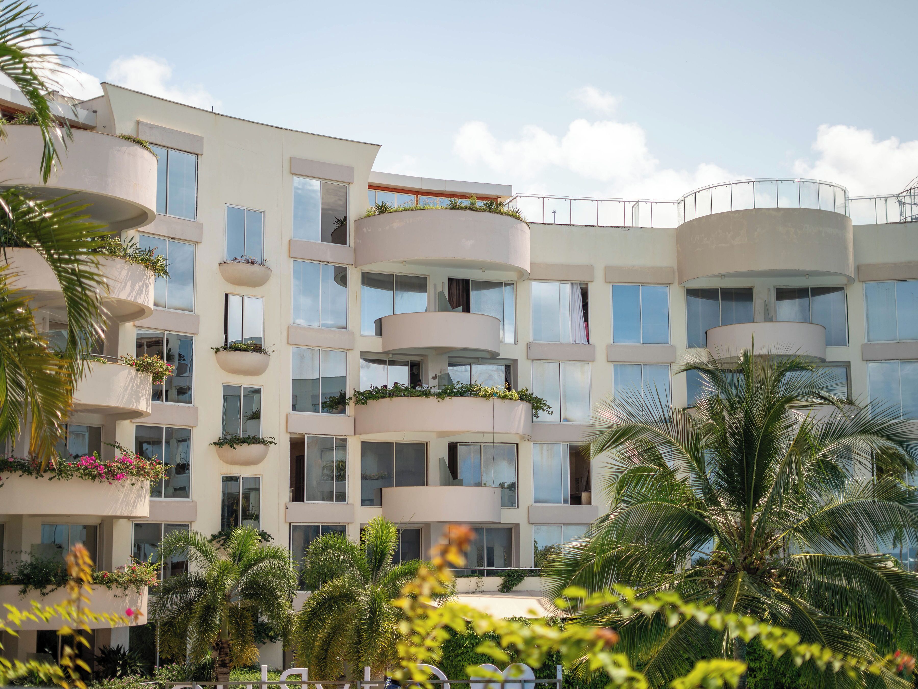 A multi-story hotel with balconies, large windows, and lush greenery.