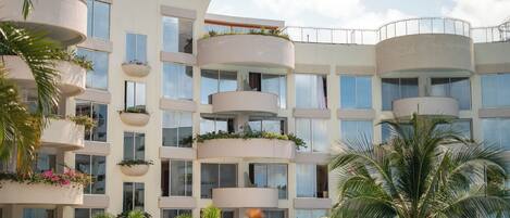 A multi-story hotel with balconies, large windows, and lush greenery.