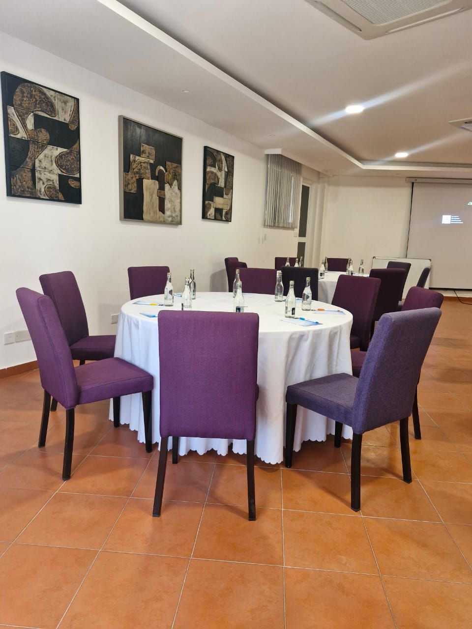 A conference room with round tables, purple chairs, white tablecloths, and artwork on the walls.