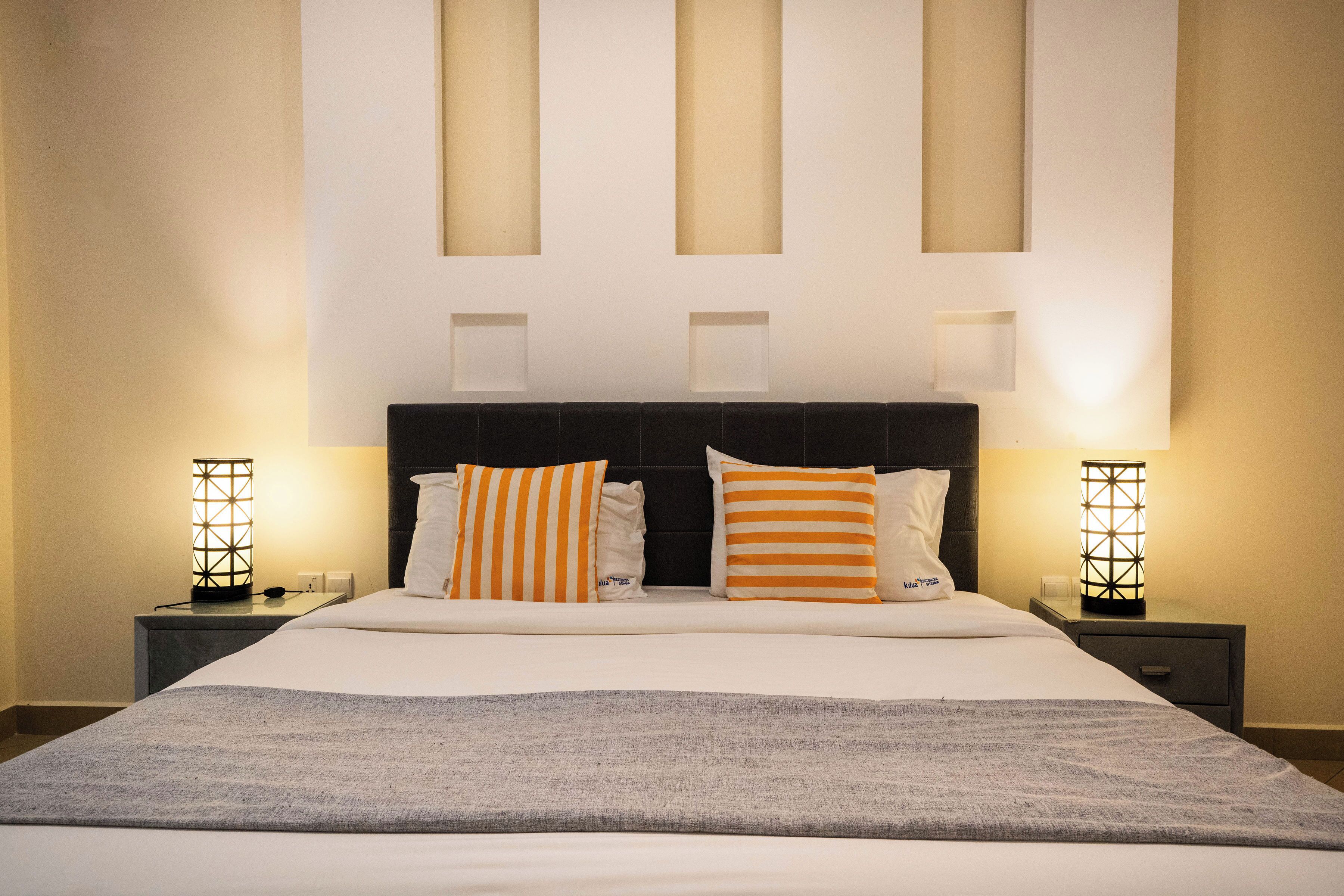 A neatly made bed with a grey blanket, two bedside tables with lamps, and a headboard with three rectangular cutouts.
