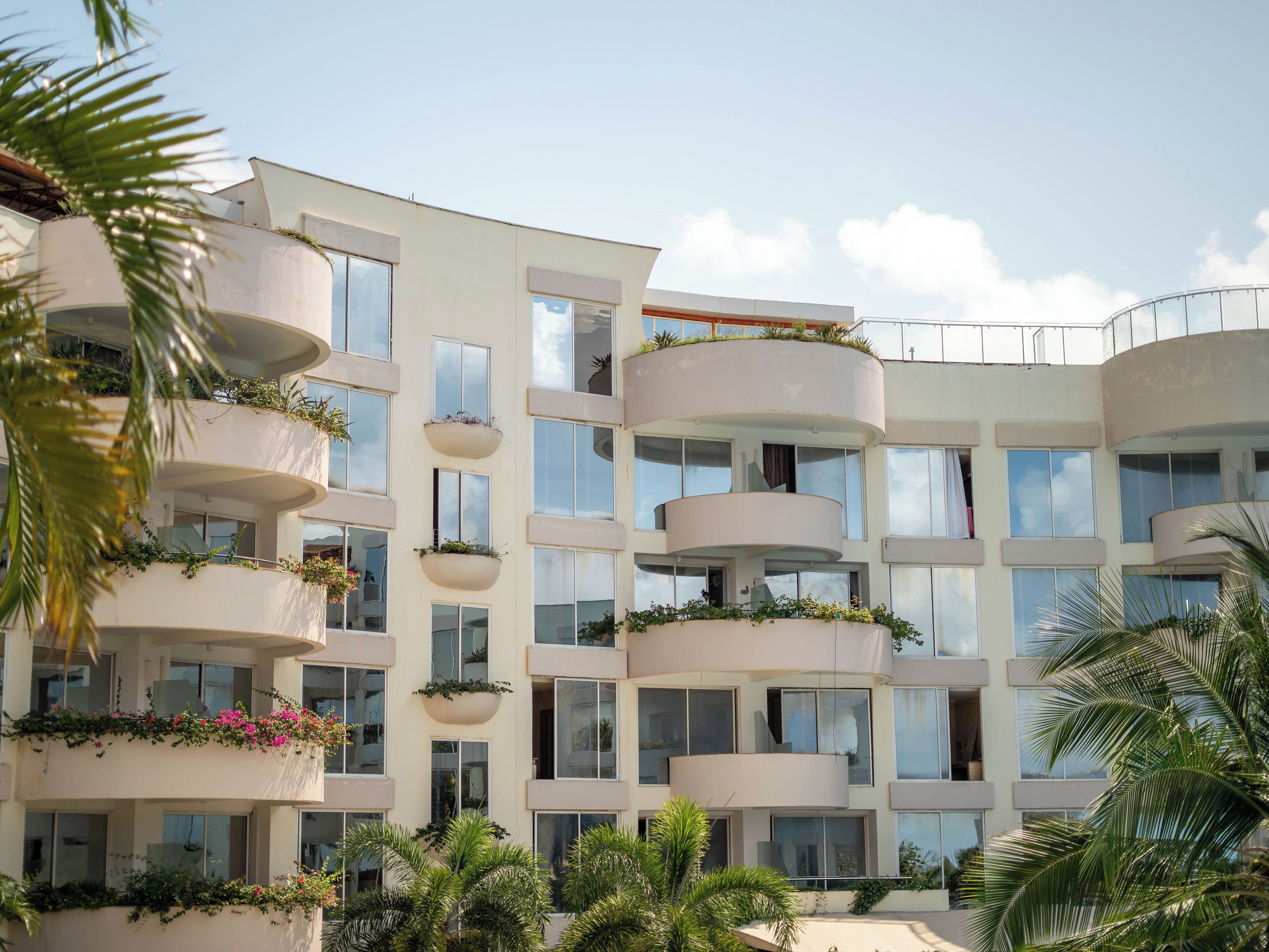 A multi-story hotel with balconies, large windows, and lush greenery.
