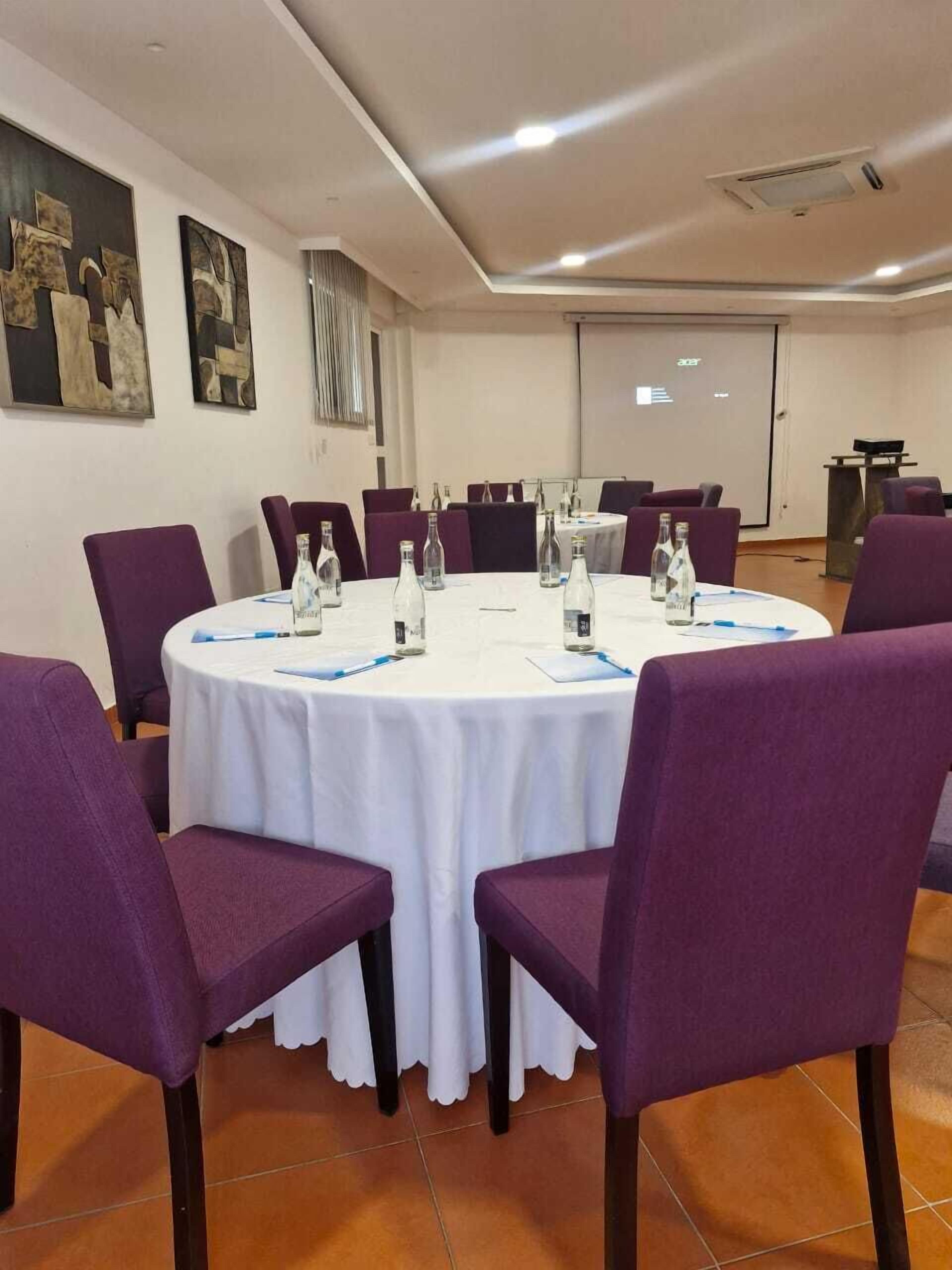 Un salón de conferencias con una mesa redonda, sillas moradas y botellas de agua sobre la mesa.