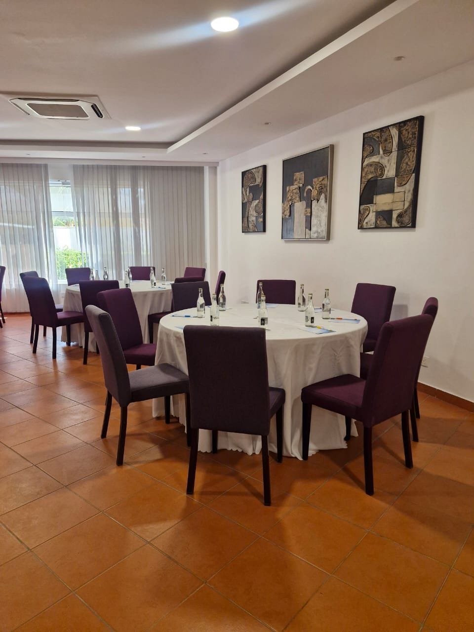 Un salón de conferencias con mesas redondas y sillas moradas, paredes blancas y arte abstracto en las paredes.