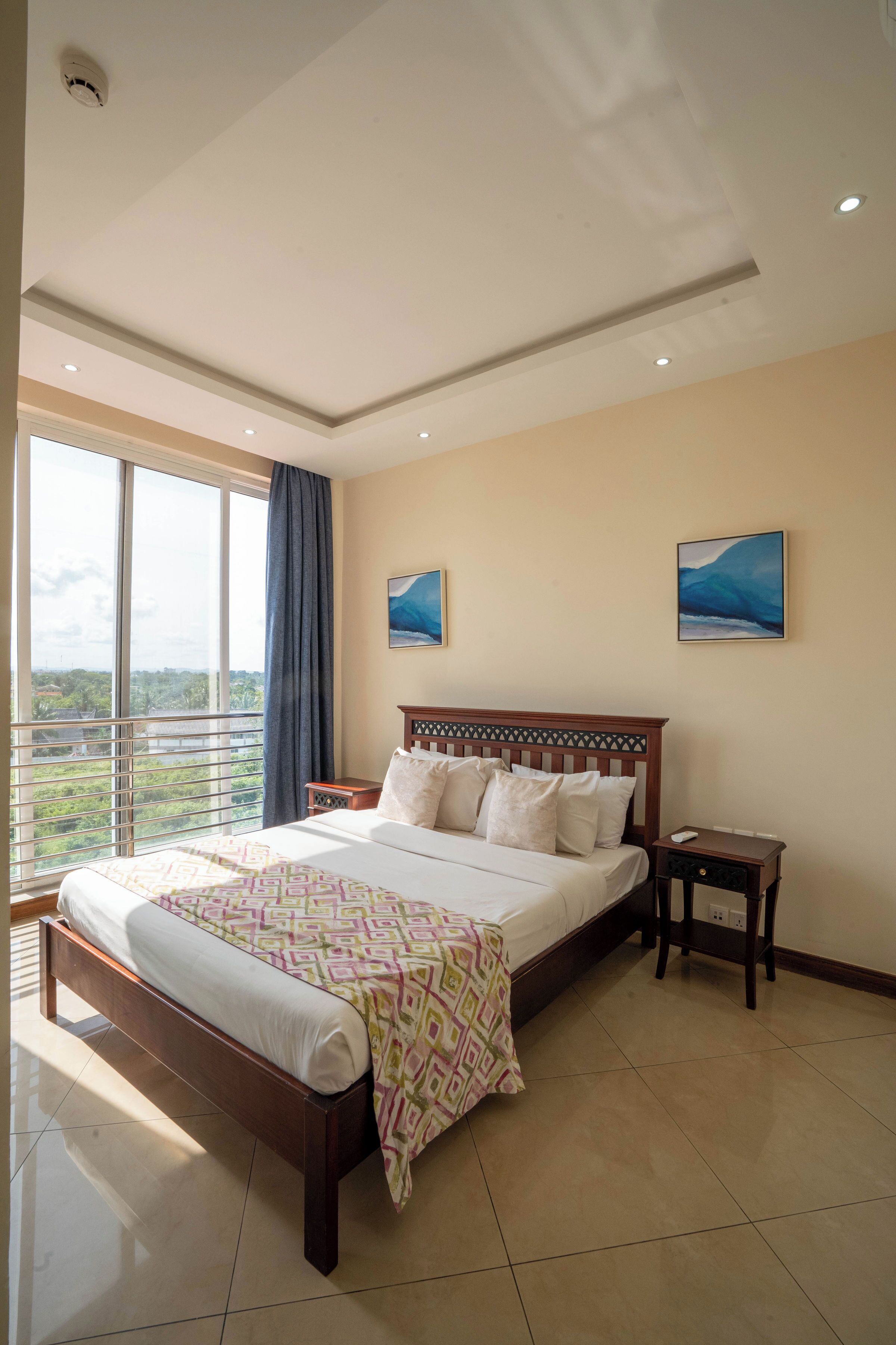 A hotel room with a large bed, a nightstand, two wall-mounted paintings, and a balcony with a view.