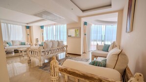 A spacious living room with a white sofa set, a wooden bench, and a large window with sheer curtains. - Kilua Residences by CityBlue, Mombasa (Mombasa)