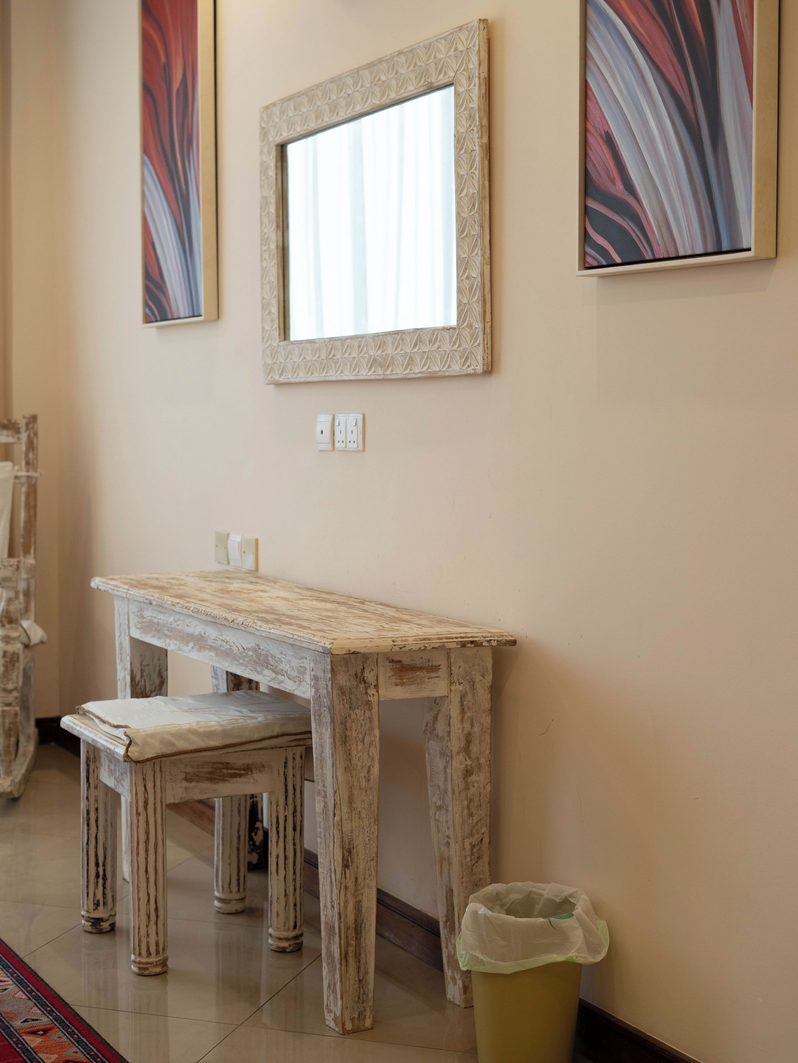 A rustic wooden table with a bench, a mirror on the wall, and a trash bin.