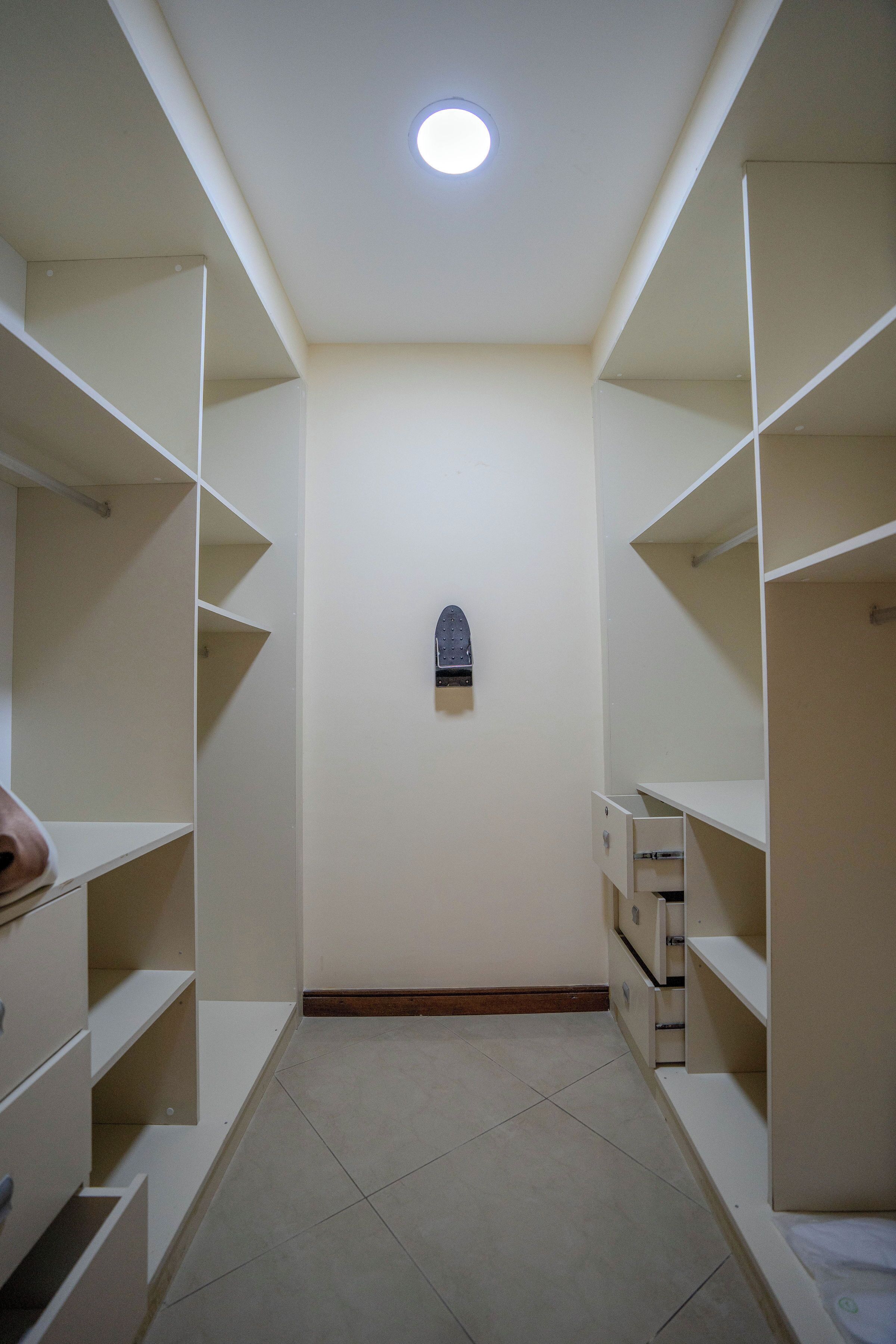 Un couloir étroit, avec des étagères blanches de part et d’autre, et un petit objet sombre accroché au mur.
