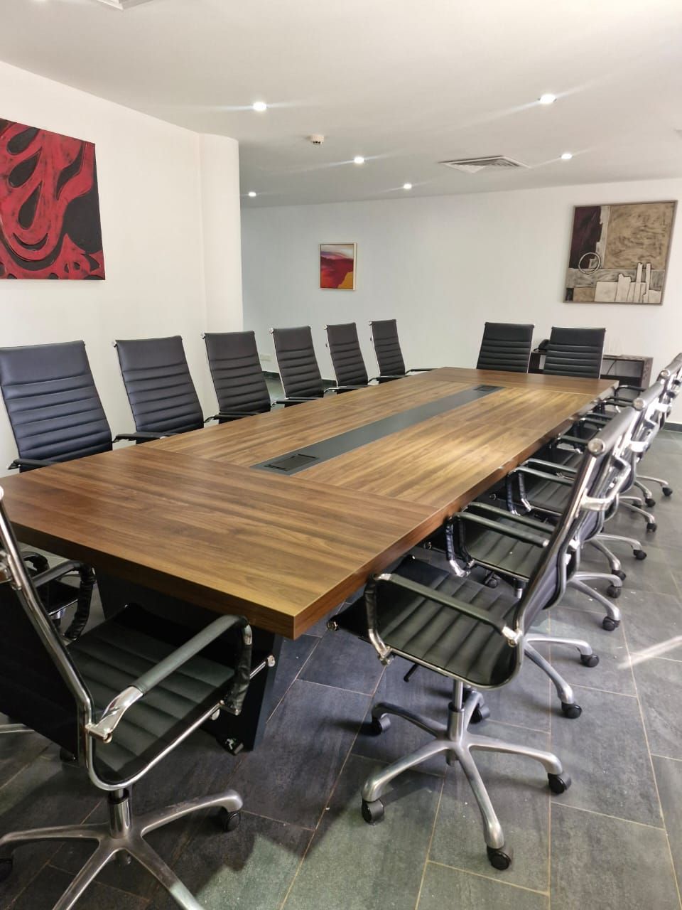 Una sala de conferencias con una larga mesa de madera, sillas de oficina negras y obras de arte en las paredes.