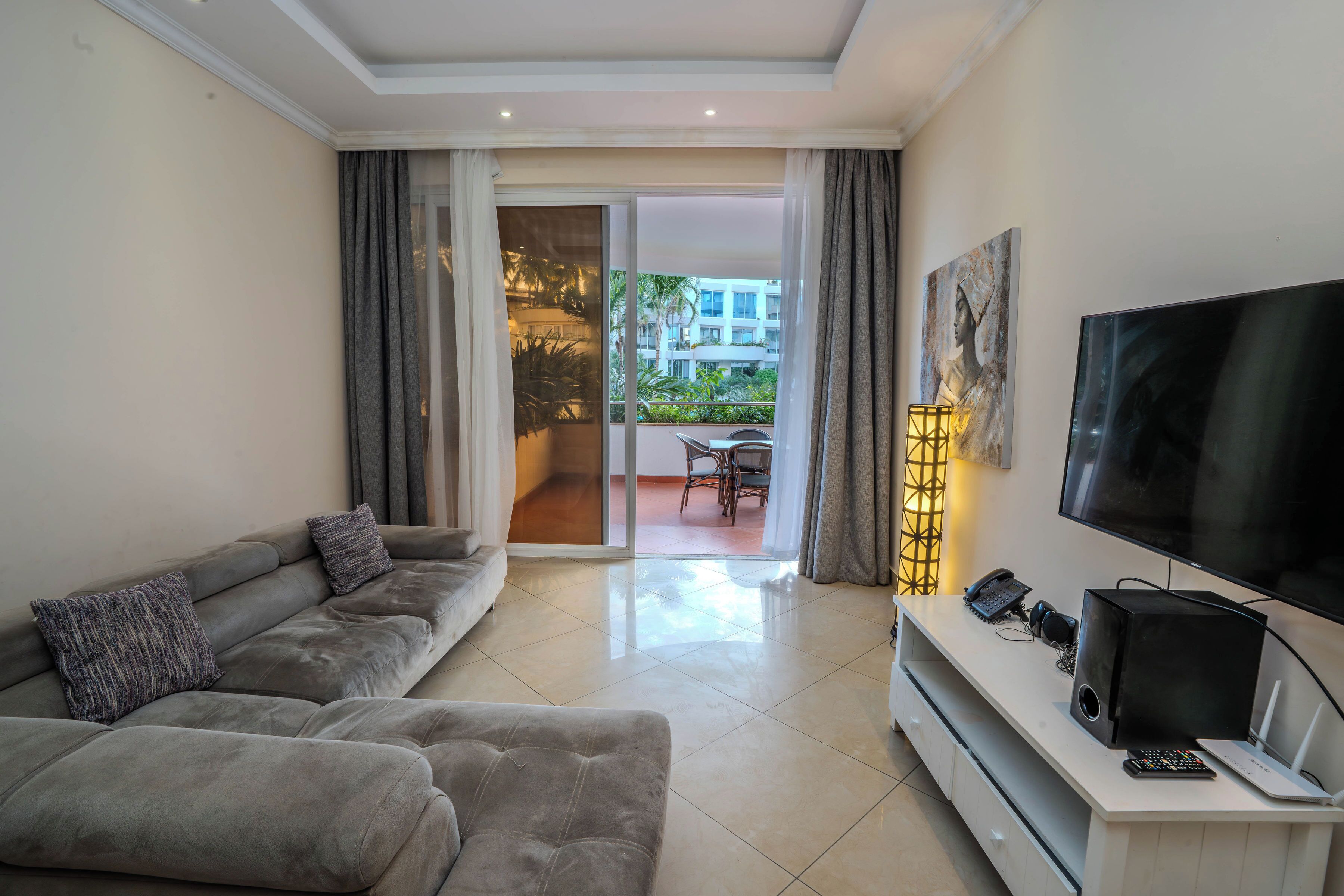 Una sala de estar moderna con un sofá gris, un televisor de pantalla plana y un mueble blanco para equipos electrónicos.