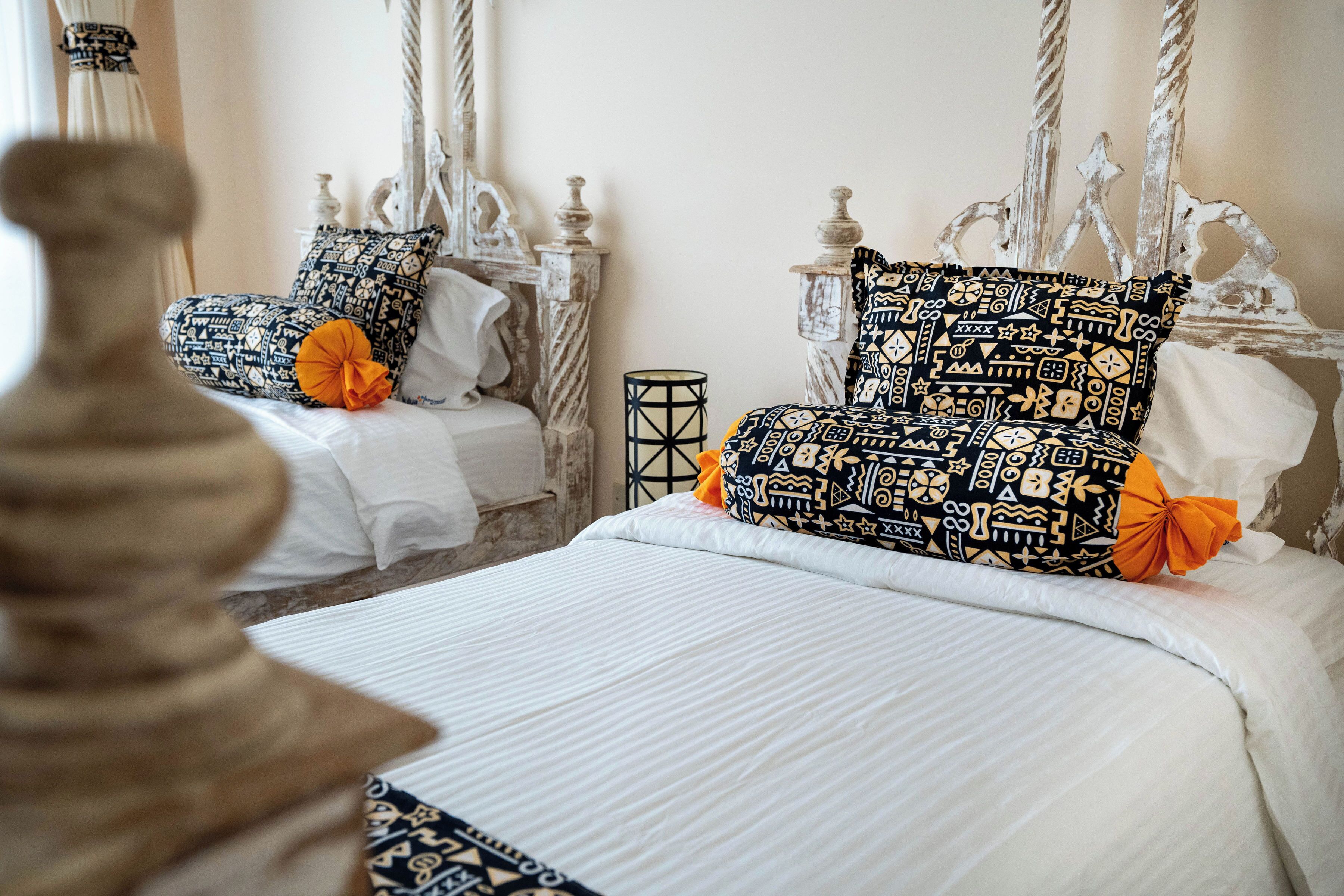A bedroom with two beds, each with patterned pillows and a small table between them.