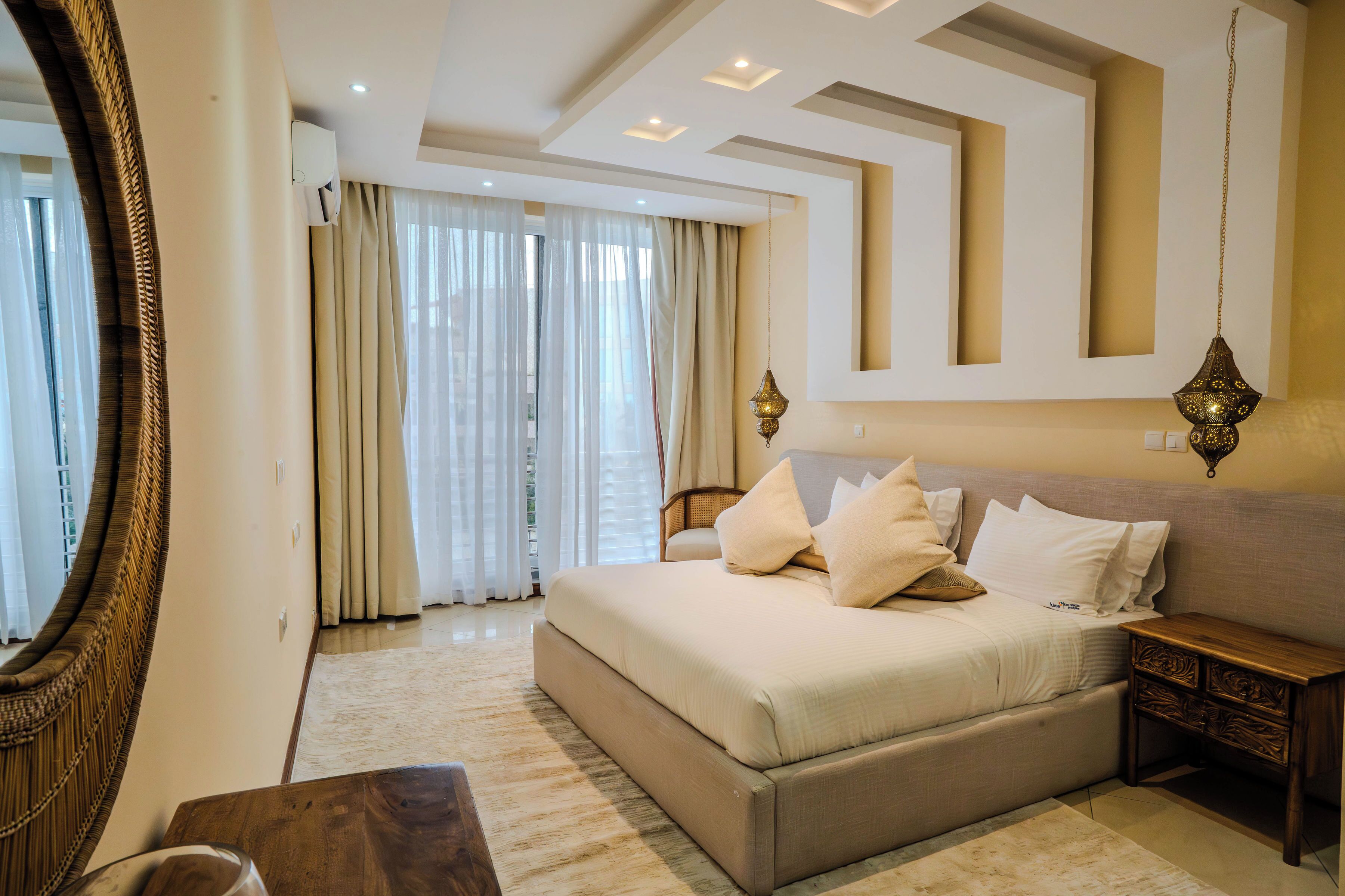 A bedroom with a large bed, a wooden nightstand, a mirror, and a ceiling with recessed lighting.