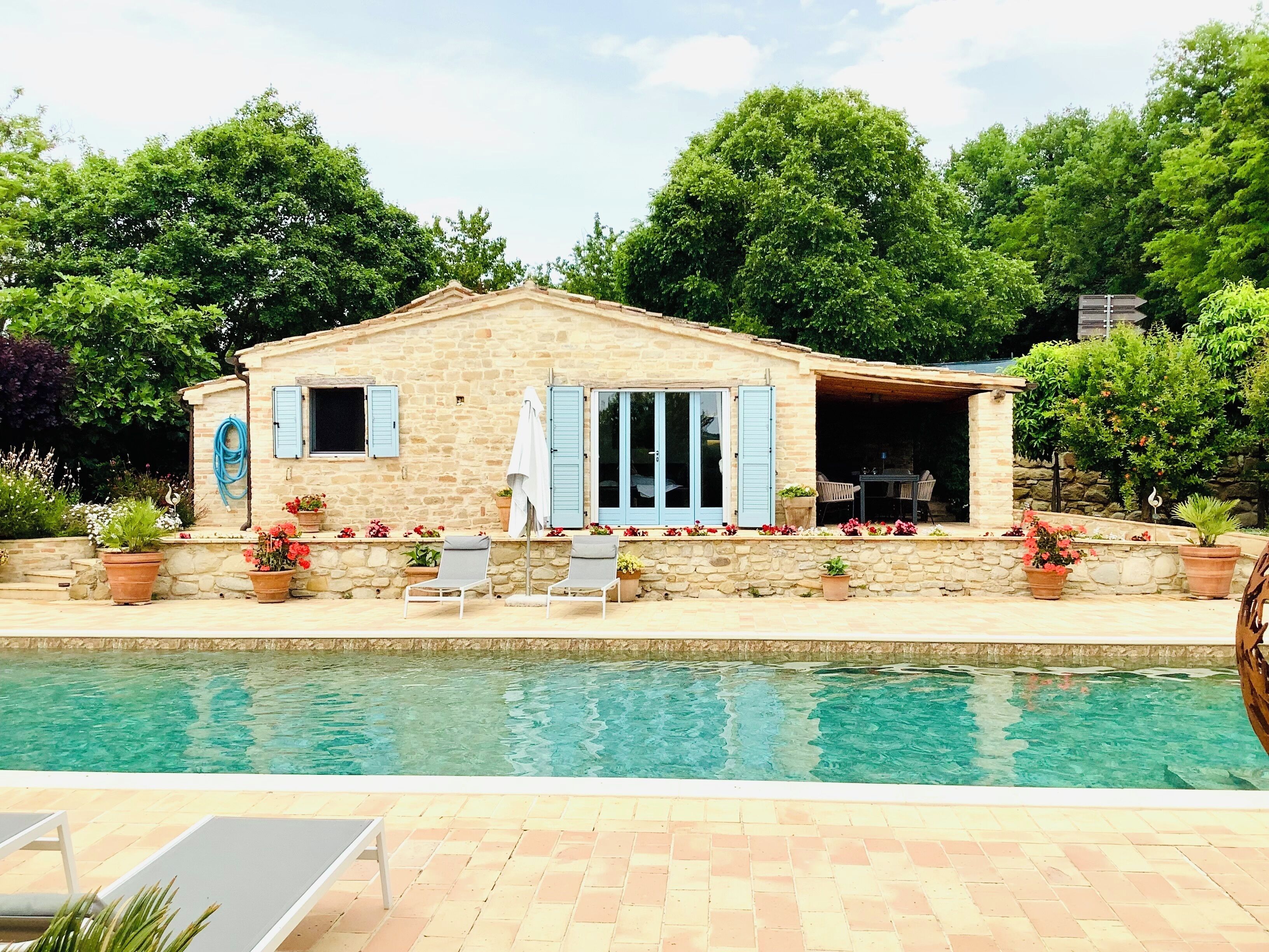 Une maison en pierre avec une piscine, deux chaises longues et un patio couvert.