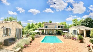 Una vila amb piscina, envoltada de vegetació exuberant i un cel blau clar.