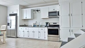 Une cuisine moderne avec des meubles blancs, des appareils électroménagers en acier inoxydable et un sol carrelé.