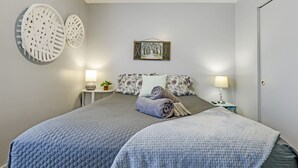Une chambre à coucher bien rangée, avec un grand lit, deux tables de chevet, un tableau accroché au mur et une porte.