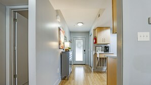 Un couloir étroit au plancher de bois, avec une porte au fond, et un coin cuisine équipé de placards et d’appareils électroménagers.