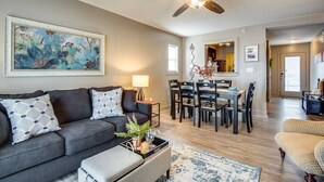 A modern living room with a dark grey sofa, a dining area with a wooden table and chairs, and a ceiling fan. - The Lofts of Downtown (540 N 2nd St, #211) (Clarksville)