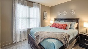 A bedroom with a bed, a nightstand, a window with sheer curtains, and decorative wall art. - The Lofts of Downtown (540 N 2nd St, #211) (Clarksville)