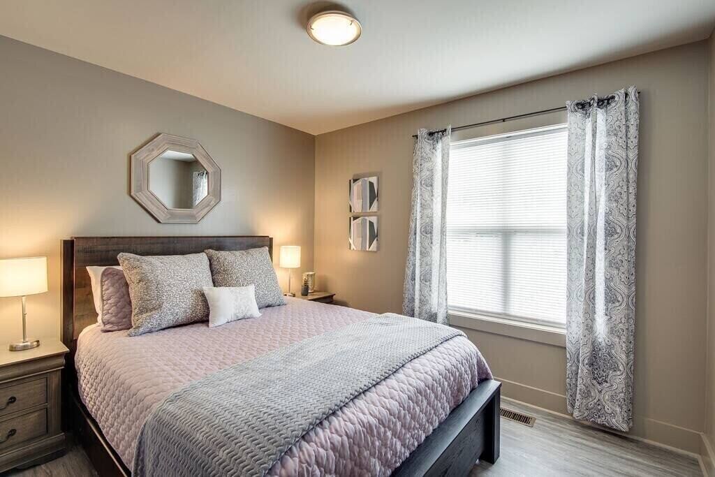 A bedroom with a bed, bedside lamps, a mirror, and a window with curtains.