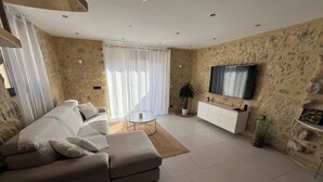 Ein Wohnzimmer mit beiger Couch, einem Couchtisch, einem Fernseher und einer Steinwand.