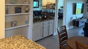 A kitchen with a granite countertop, white cabinetry, and a dining area with a wooden table and chairs. - Ocean view oasis (Jensen Beach)