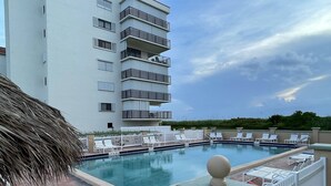 A rooftop pool with lounge chairs, a thatched umbrella, and a white fence. - Ocean view oasis (Jensen Beach)