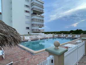 A rooftop pool with lounge chairs, a thatched umbrella, and a white fence. - Ocean view oasis (Jensen Beach)