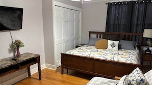 A bedroom with a wooden bed, a desk, a chair, a TV, and a door. - Twin Porch Retreat (Cambridge)