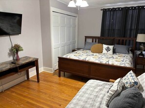 A bedroom with a wooden bed, a desk, a chair, a TV, and a door.