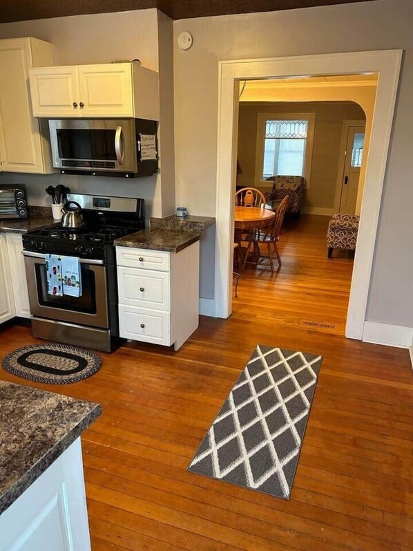 A kitchen with white cabinets, a microwave, a stove, and a dining area with a table and chairs.