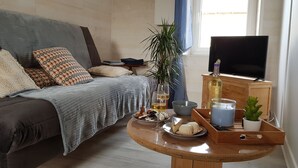 Ein gemütliches Schlafzimmer mit einem Bett, einem Fernseher, einem kleinen Tisch mit Snacks, einer Pflanze und einem Fenster.
