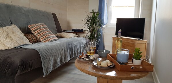 A cozy bedroom with a bed, a TV, a small table with snacks, a plant, and a window.