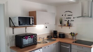 Eine kompakte Küche mit Mikrowelle, Toaster, Kaffeemaschine und Geschirrspüler. Darüber befinden sich Holzregale und eine dekorative Wandsticker.