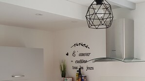 Eine moderne Küche mit Holzarbeitsplatte, einer schwarzen Hängeleuchte und einem an der Wand montierten Regal mit Küchenutensilien.