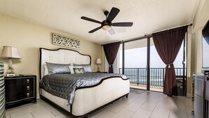 A spacious bedroom with a large bed, a ceiling fan, a nightstand, and a view of the ocean through a sliding glass door. - Ashley Collection (Daytona Beach Shores)