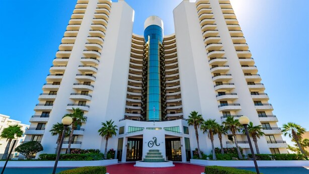 A high-rise hotel with a central blue tower, multiple balconies, and a red pathway leading to the entrance. - Ashley Collection (Daytona Beach Shores)