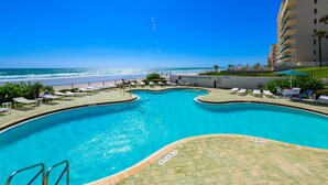 A pool with a view of the beach and ocean, surrounded by lounge chairs and a building. - Ashley Collection (Daytona Beach Shores)