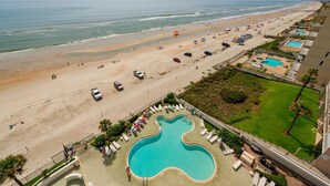A beachside hotel with a pool shaped like a guitar, a parking lot, and a view of the ocean. - Ashley Collection (Daytona Beach Shores)