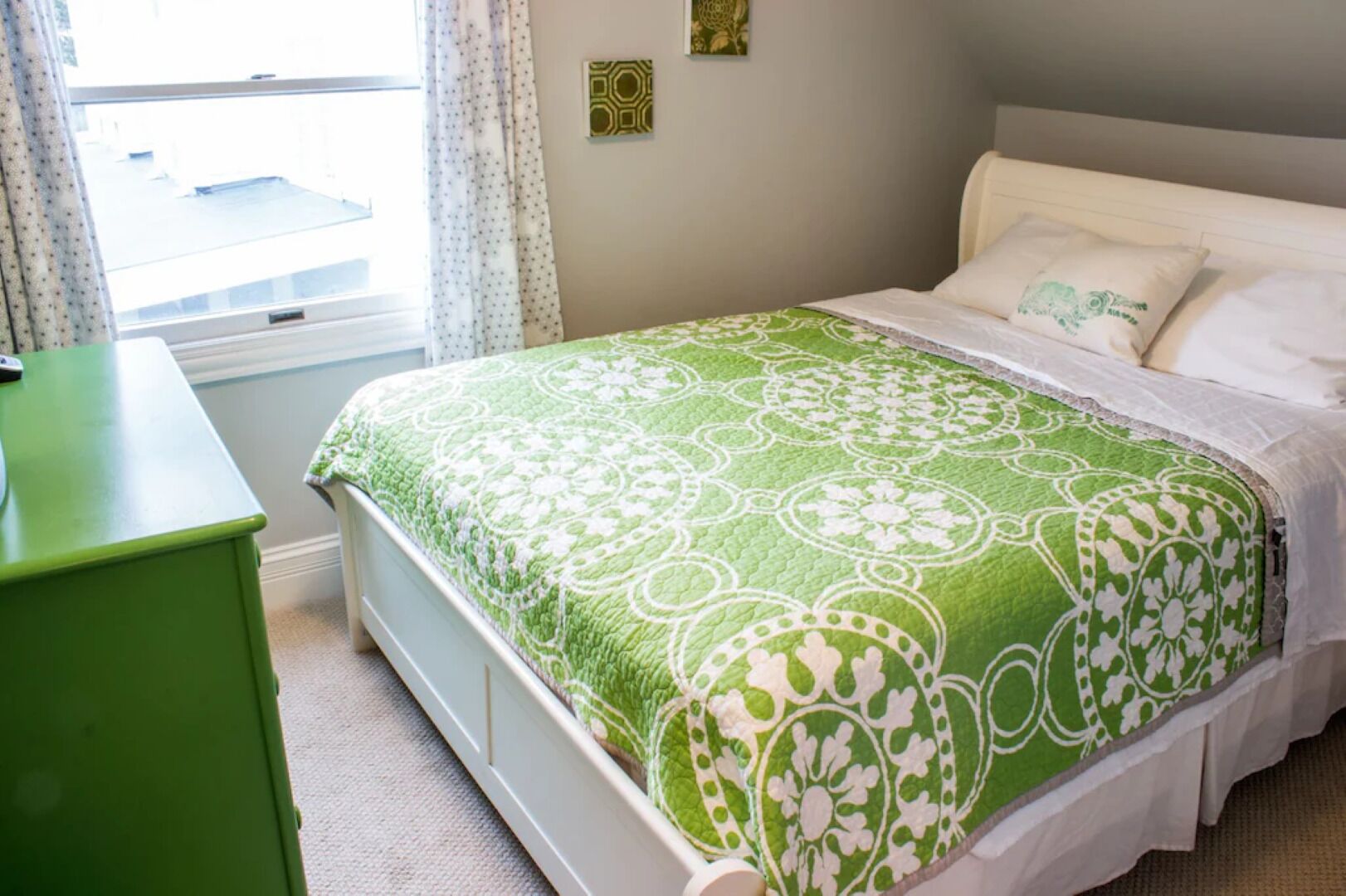 Een slaapkamer met een bed, een groene dressoir, een raam met gordijnen en een wandlamp.