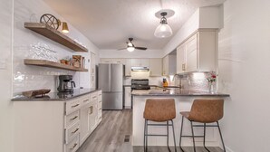 A modern kitchen with white cabinets, a double-door refrigerator, a coffee maker, and two bar stools.