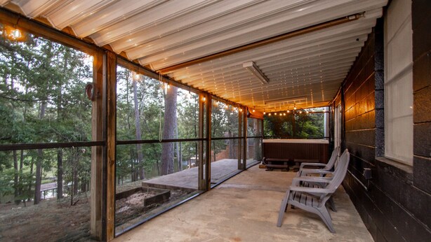 A covered outdoor seating area with benches and string lights, large windows offering forest views.