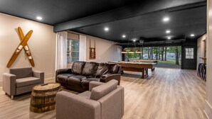 A modern living room with a pool table, leather sofa, and skis on the wall.