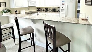 A modern kitchen with white cabinets, a granite countertop, and two bar stools.