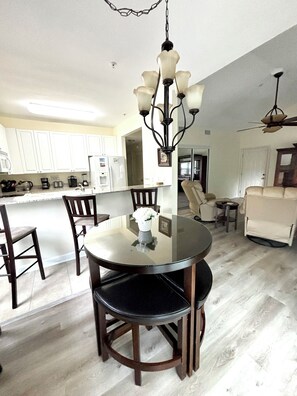 A dining area with a round table, four chairs, and a chandelier. - Lovely 2-bedroom condo with pool (Gulf Shores)
