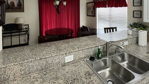 A kitchen with granite countertops, a stainless steel sink, a chandelier, and red curtains.