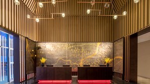 A modern reception area with a wooden slatted ceiling, two reception desks with red backlit edges, and a large wall mural with gold leaf accents. - Ramada Plaza by Wyndham Xiangtan Wanlou (Xiangtan)