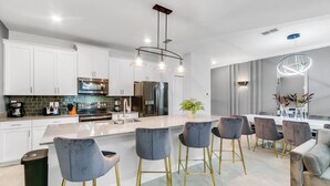 Uma cozinha moderna com armários brancos, eletrodomésticos de aço inoxidável e uma ilha central com banquetas.