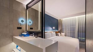 A modern hotel room with a large bed, a bathroom with a vanity, and a large mirror. - Novotel Dongguan Songshan (Dongguan)