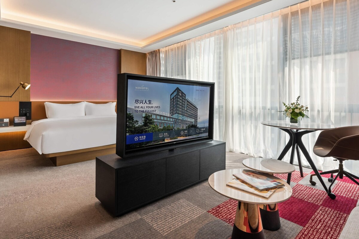 Una habitación de hotel moderna con una cama, un televisor de pantalla plana sobre un mueble, una mesita redonda y una silla.